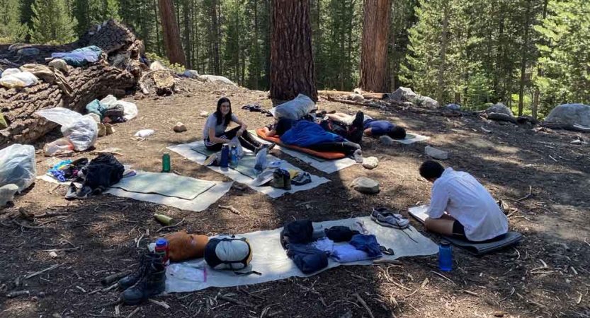 a group of students rest on pads in a wooded area during a backpacking course with outward bound